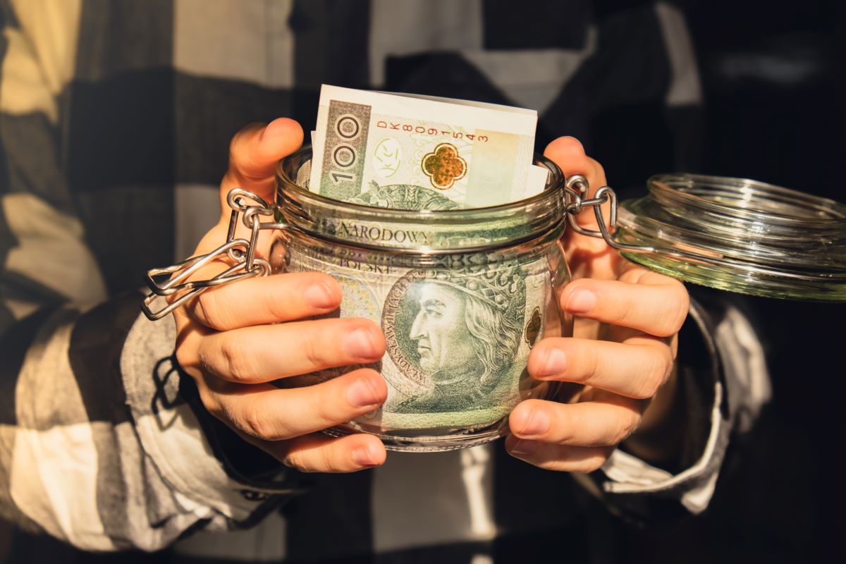 Człowiek trzyma słoik z polskimi banknotami.