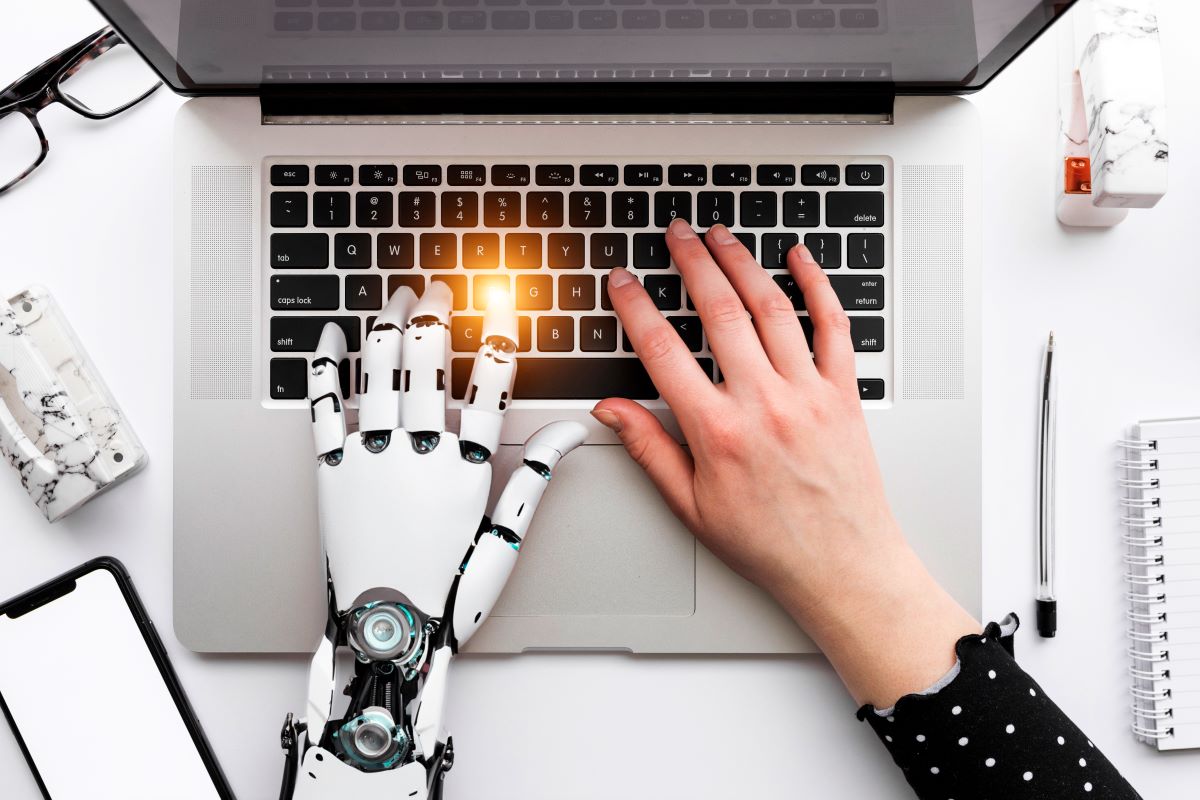 Ręka człowieka i robota pracujące na laptopie.
